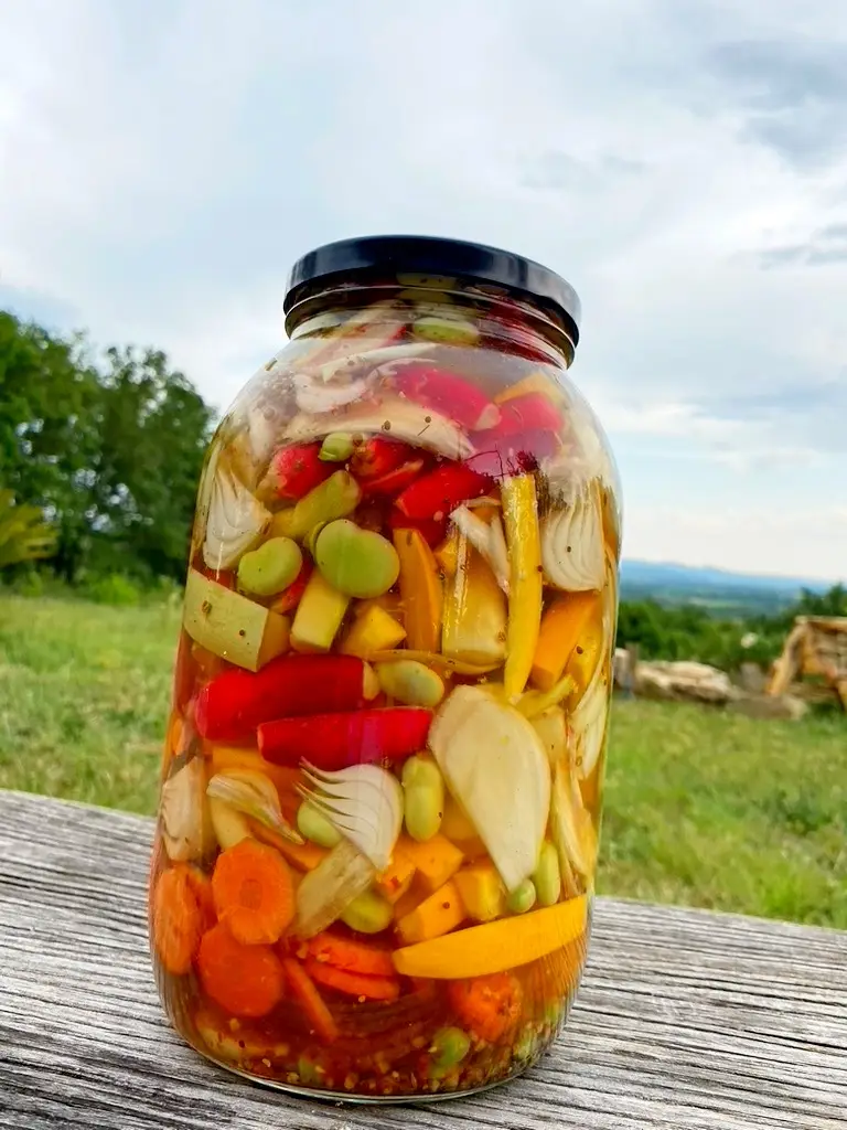 Bocal de pickles fait maison sur une table en bois en extérieur avec une vue sur le jardin.