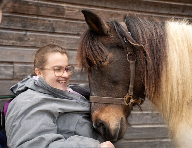 Jeune fille souriante avec un cheval frottant sa tête contre elle durant un atelier d'équi-handi au mas de rivet à Barjac.