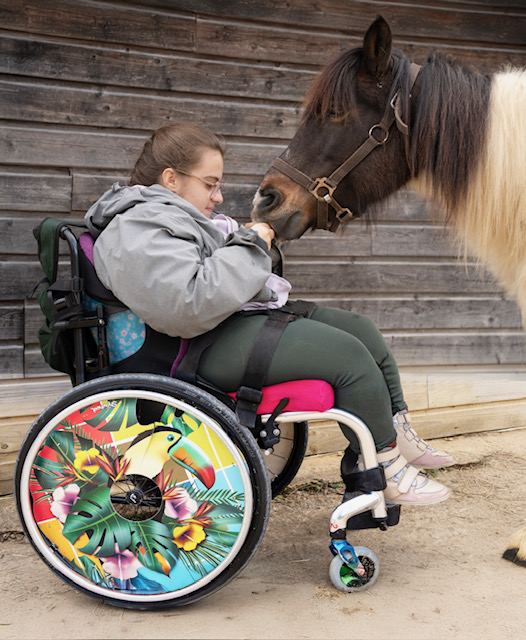 Jeune fille en fauteuil roulant avec cheval posant son museau sur ses mains durant en atelier d'équi-handi à l'association les enfants extraordinaires à Barjac.